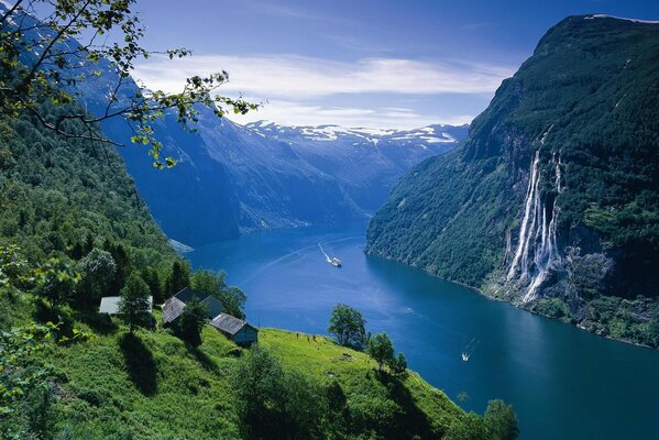 Ein Bergfluss in Norwegen von unbeschreiblicher Schönheit mit kleinen Häusern auf grünen Feldern und Wasserfällen, die in den Fluss münden