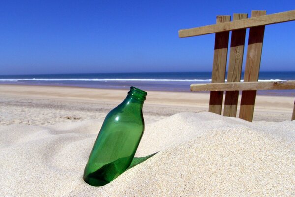 Im Sand steckende leere Flasche am Meeresufer