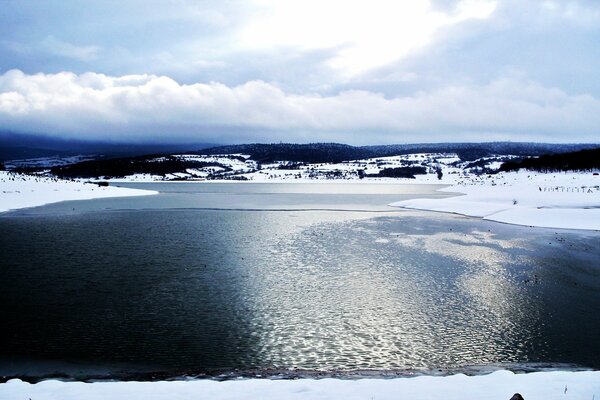 Hermoso lago de invierno con orillas cubiertas de nieve bajo los rayos del sol