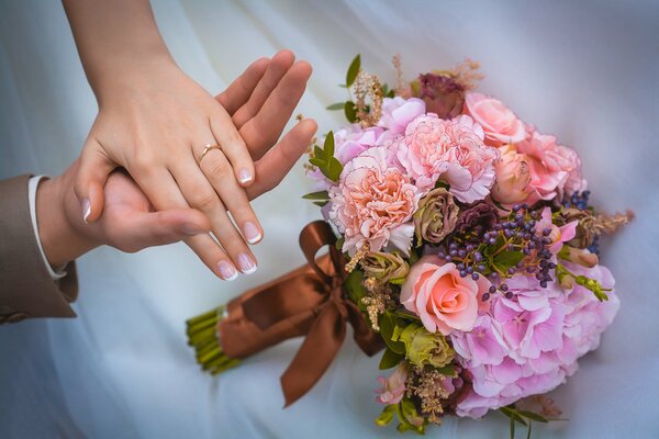 The hands of the newlyweds and the wedding bouquet