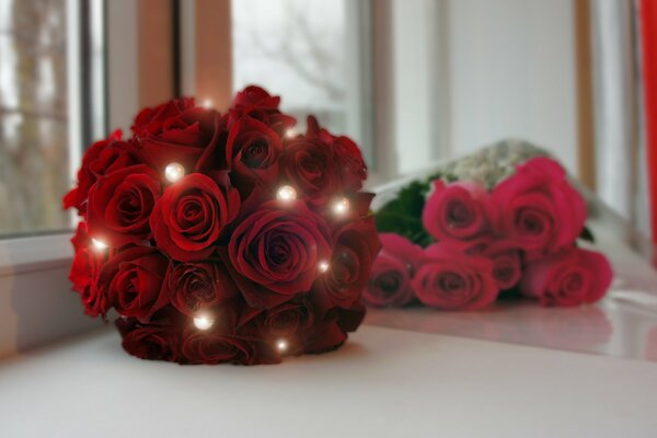 Un ramo de rosas escarlatas y un ramo de rosas rojas se encuentran en el alféizar de la ventana