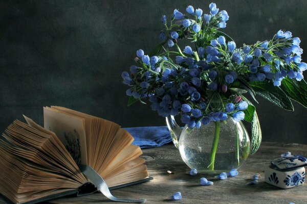 Fleurs bleues dans un vase sur une table et un livre ouvert