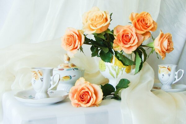 Nature morte. Bouquet de roses et un ensemble de thé sur une nappe blanche comme neige