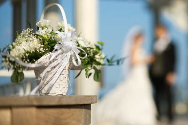 Cesto di fiori bianchi da sposa con nastro bianco su sfondo sfocato sposa e sposo