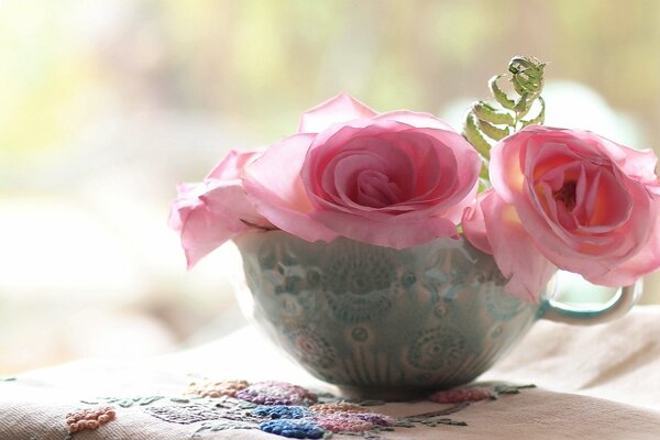 Tazza con rose vicino al tovagliolo ricamato