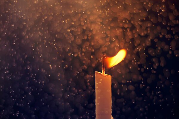 A burning candle against the background of raindrops