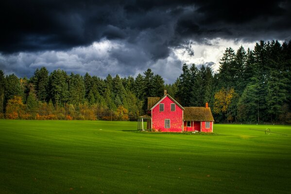 Casa roja en medio de un campo verde con un cielo oscuro