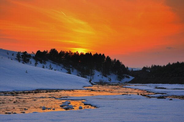 Winter river against the background of dark trees and the amazing beauty of a bright sunset on a wonderful winter evening