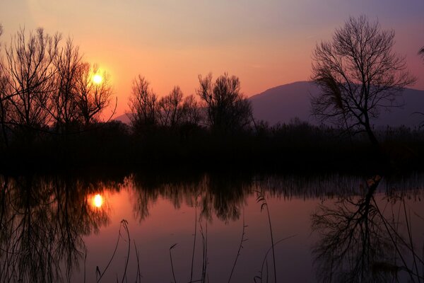 El sol naranja al atardecer se refleja en el lago