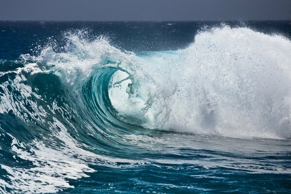 A high foam wave with splashes in the middle of the ocean and a gray sky on the horizon