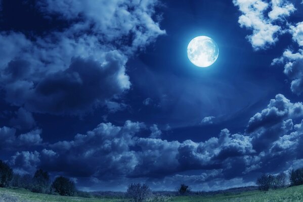 Luna llena en el cielo con nubes sobre el campo verde