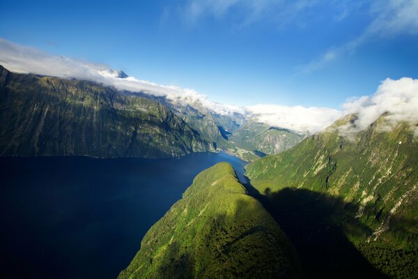 Green hills with snowy peaks and blue cold water at the foot