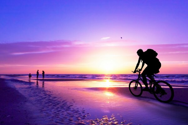 L uomo va in bicicletta lungo la spiaggia al tramonto