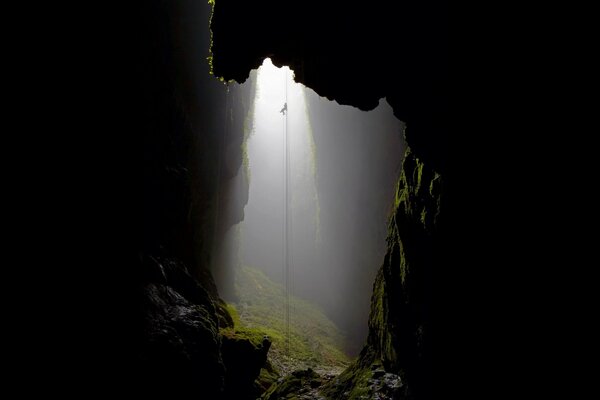 A rope lowered into a cave overgrown with moss