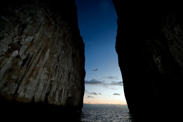 A rift in the rock through which a bird flying by is visible