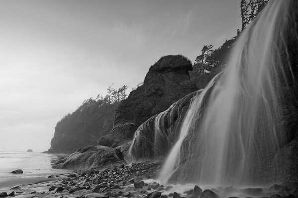 Eine Tapete in schwarz-weißen Farben, in der sie von einem Wasserfall umgeben sind, der auf Steine fällt und am Ufer ins Meer abfließt