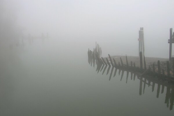 Das Ufer ist in Nebel gehüllt. Neben dem kaputten Zaun