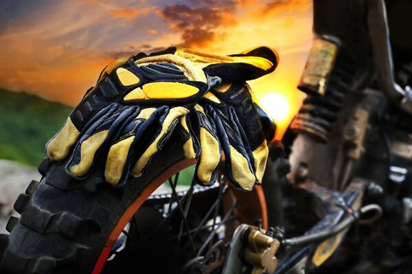 Yellow motorcycle gloves on a motorcycle on the background of the setting sun