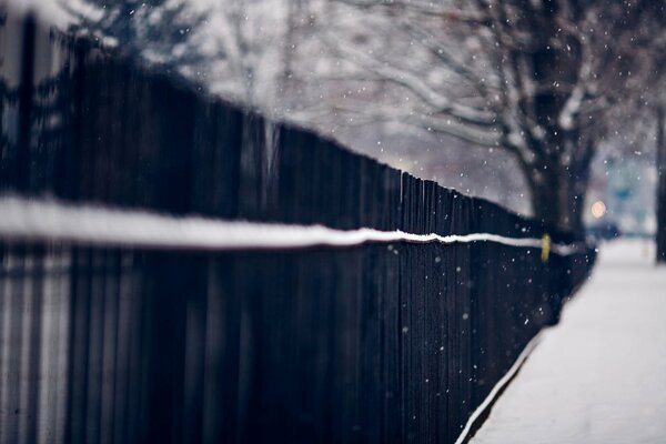 Lungo recinto nero lungo la strada innevata