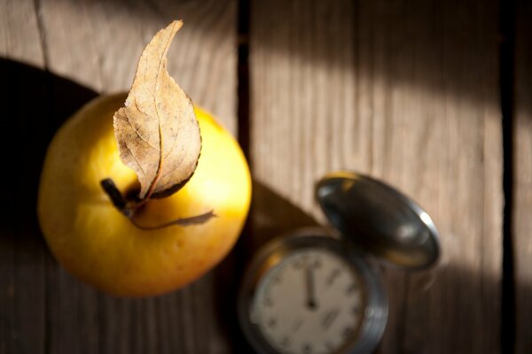 Apfel mit Blatt und Uhr auf Holztisch