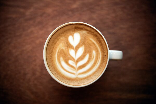 A cup of cappuccino coffee with foam and a flower pattern with a heart