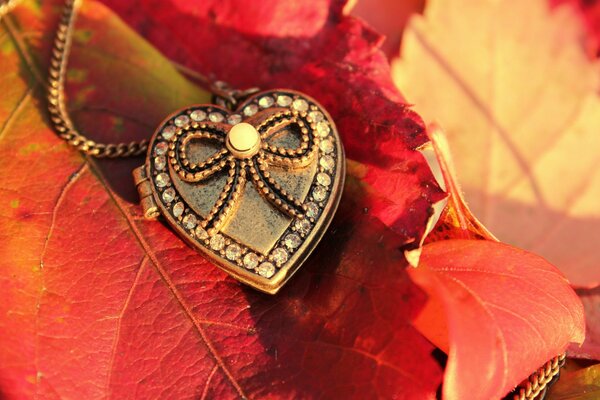 A heart-shaped keychain decorated with a bow lies on an autumn leaf