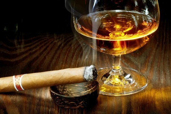 A cigar with a house next to cognac in a glass