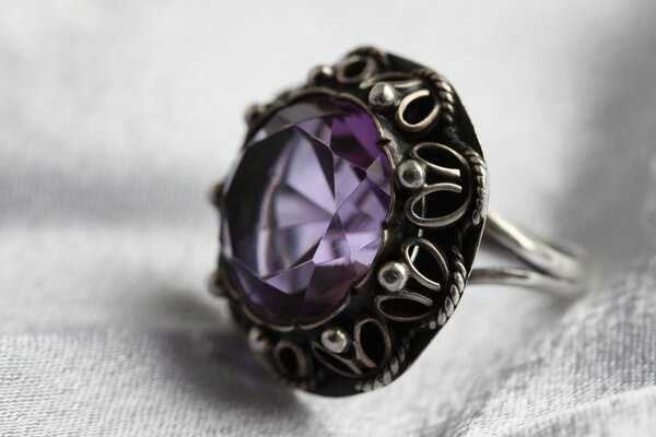 A silver metal ring with a purple stone on a gray fabric background