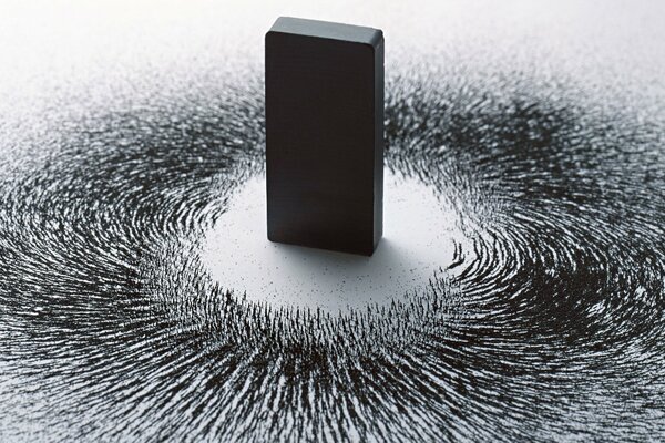 Black magnet on a white background with metal filings around