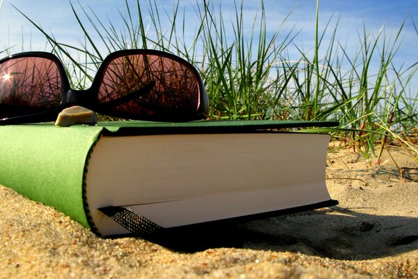 Sonnenbrille und Buch im Sommer am Sandstrand zurückgelassen