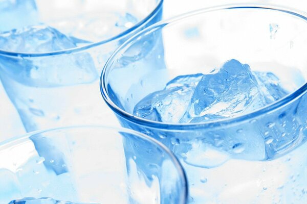 Three clear glass glasses with clear liquid and ice in blue tones