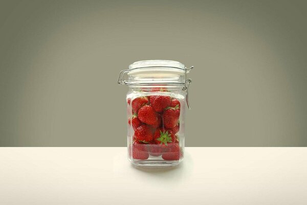 A glass jar with strawberries closed with a lid on the table