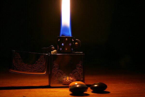 A metal lighter with a lit flame standing on the table in an orange glow