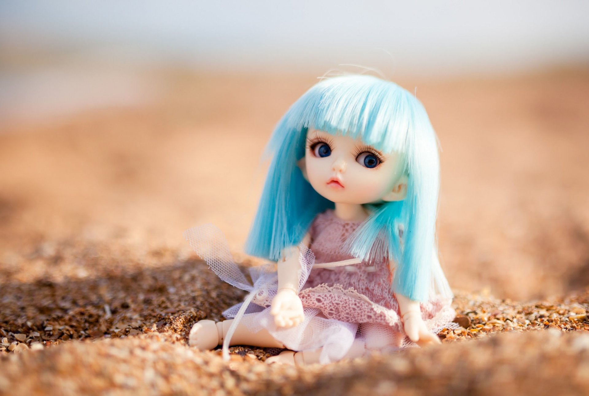 puppe spielzeug blaues haar sitzt sand