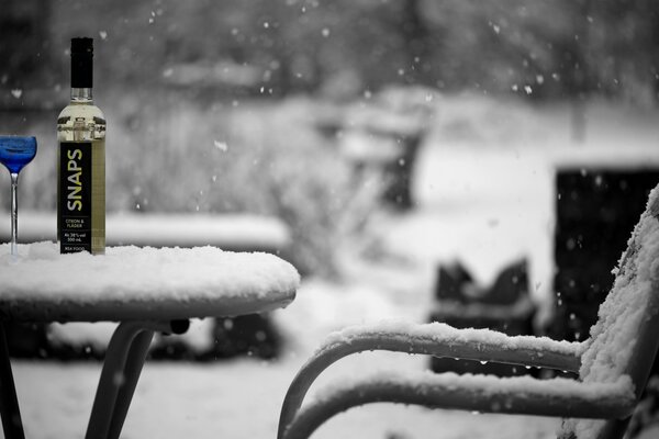 An open cafe with a snow-covered chair and a table with alcohol on it