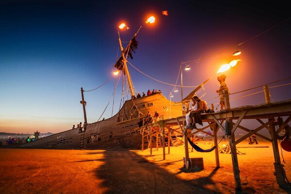 At sunset, a sinking ship with a burning mast and people on deck
