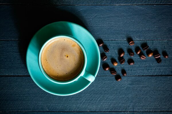 Caffè in una tazza su un piattino su uno sfondo di tavole blu scuro e chicchi di caffè