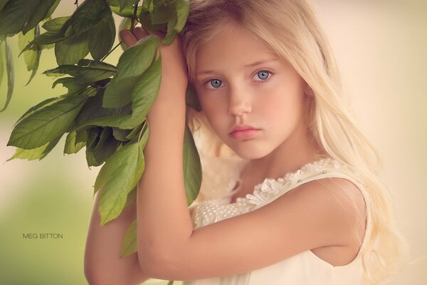 La niña se aferra a una rama con hojas verdes