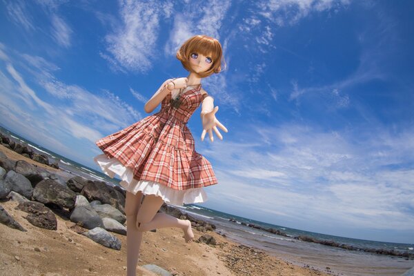 Doll toy in a dress on the beach near the sea