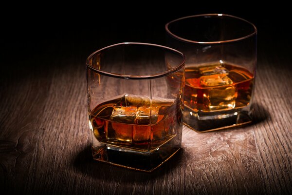Due bicchieri di whisky con ghiaccio su un piano di lavoro in legno