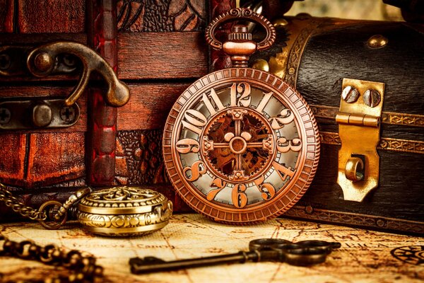Eine alte Uhr steht auf dem Tisch. Daneben liegen eine Taschenuhr und ein alter Schlüssel