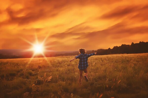 A boy runs across a field in the rays of the sun