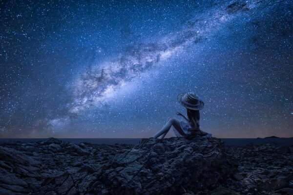 Chica en las rocas en el fondo del mar bajo el cielo nocturno