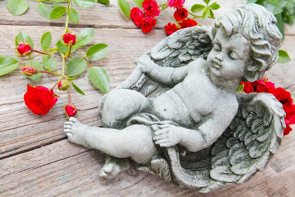 Figura di angelo di Cupido sul tavolo con rose rosse