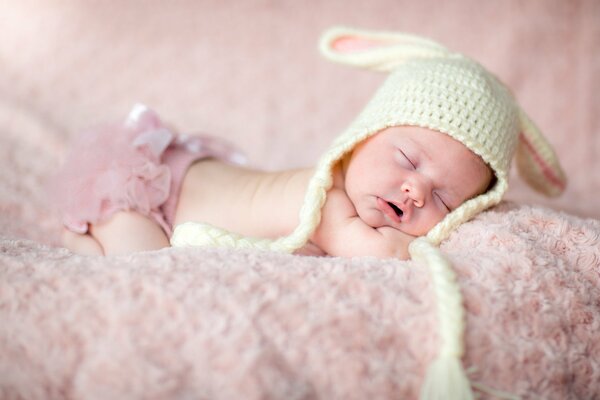 A newborn baby is lying on the bed in a hat