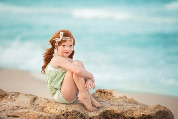 A red-haired girl is sitting on the sand somewhere near the sea