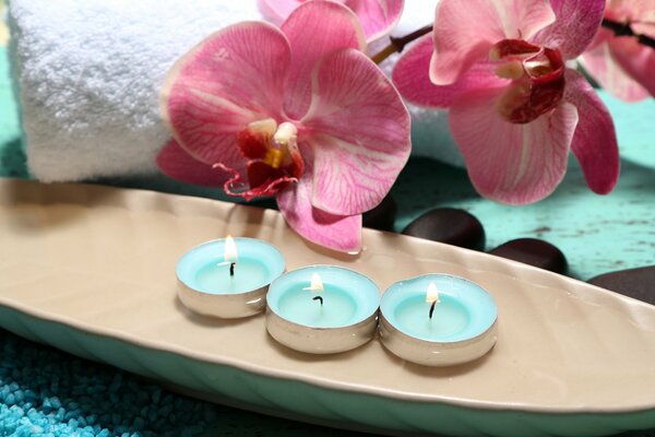 Tre candele accese. Sullo sfondo un asciugamano bianco e orchidee
