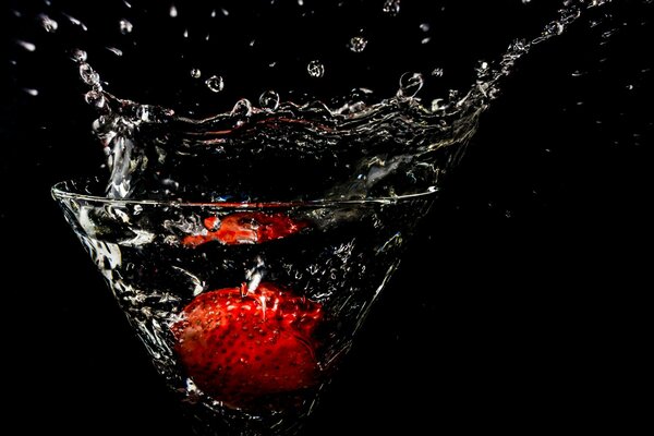 Fraises dans un verre de vin sur un fond noir avec des éclaboussures