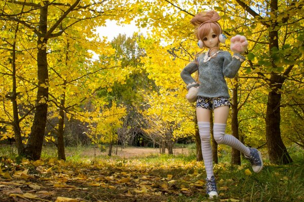 A toy doll in headphones and sneakers on the background of an autumn park