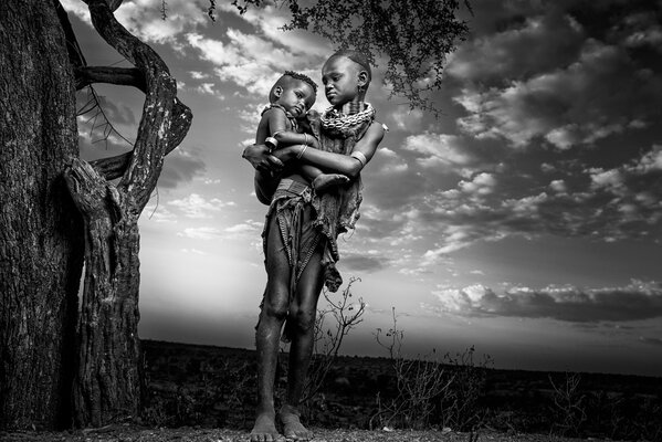 Afrikanische Mutter mit Reiank neben einem Baum